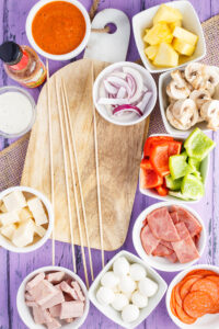 All the ingredients you need for pizza kabobs laid out in white bowls