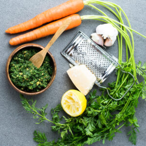 All the ingredients you need for carrot top pesto laid out on the table including parmesan  cheese, lemon, garlic.