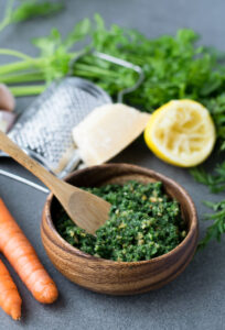 Carrot top pesto in a brown bowl with a wooden spoon