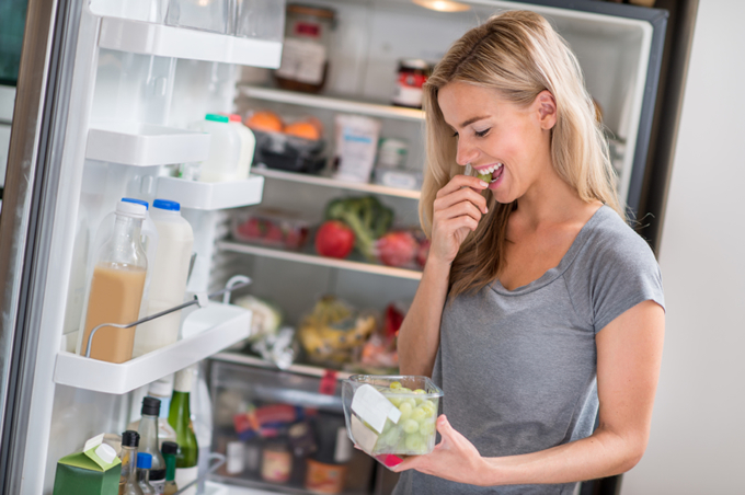 woman eating grapes in front of open fridge